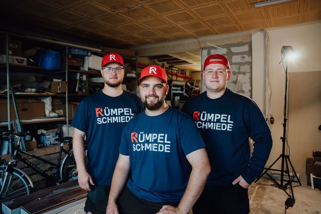 Drei Mitarbeiter der Rümpelschmiede in einem Raum mit Regalen
